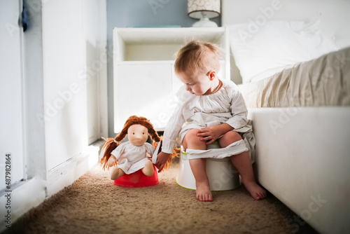 Fotografia Cute caucasian kid with doll sit on potty in bedroom, concept of hygiene and pot