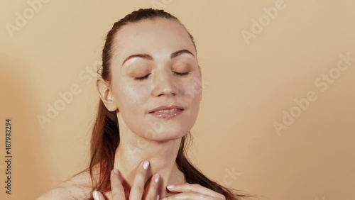 Attractive caucasian girl with smooth and clean skin is massaging her face isolated on a beige studio background. Skin care concept.