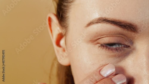 Close-up of an attractive caucasian girl massaging the skin under the eye isolated on a beige studio background. Skin care concept.