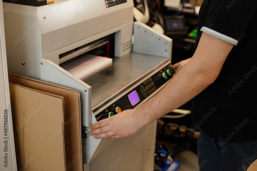 Cropped image man hands using paper cutter machine, guillotine offset. Control panel,set up laser cut level. Manufacture Cropped image man hands using paper cutter machine, guillotine offset. Control panel,set up laser cut level. Manufacture