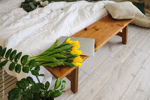 Yellow tulips and laptop on wooden bench in bedroom #487984623