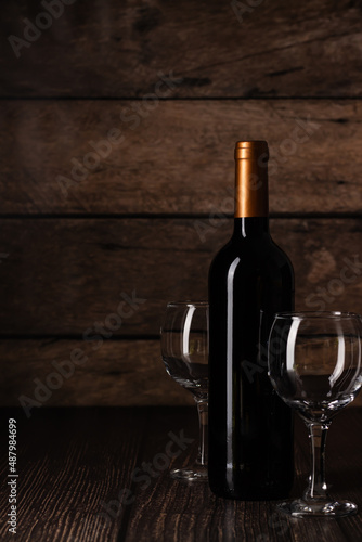 Bottle of wine with two glasses set against wooden texture, ideal for wine-related promotions.
