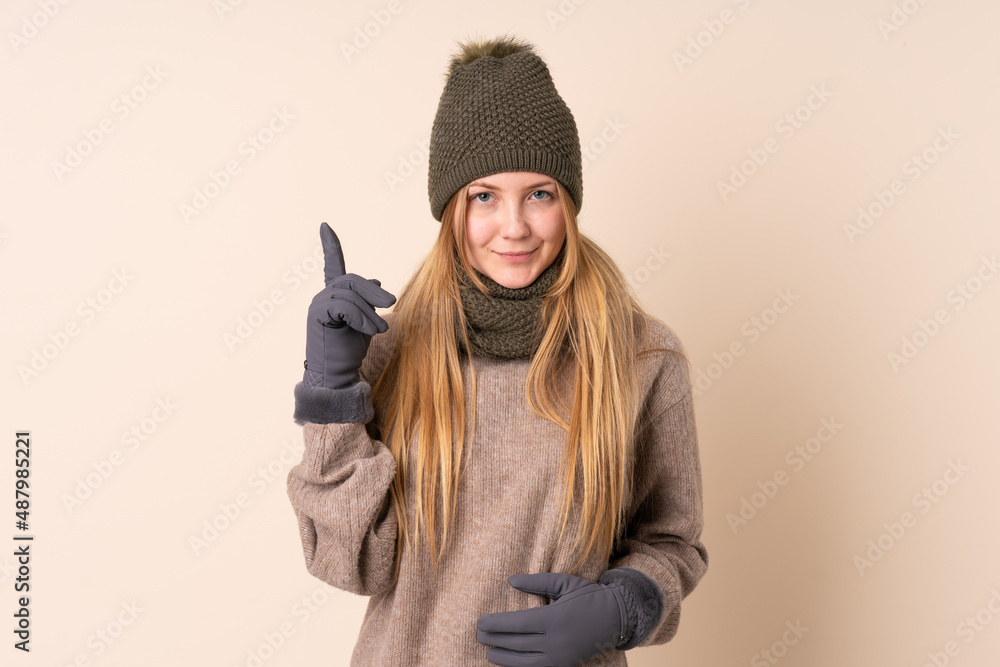 Teenager Ukrainian girl with winter hat isolated on beige background pointing with the index finger a great idea Teenager Ukrainian girl with winter hat isolated on beige background pointing with the index finger a great idea