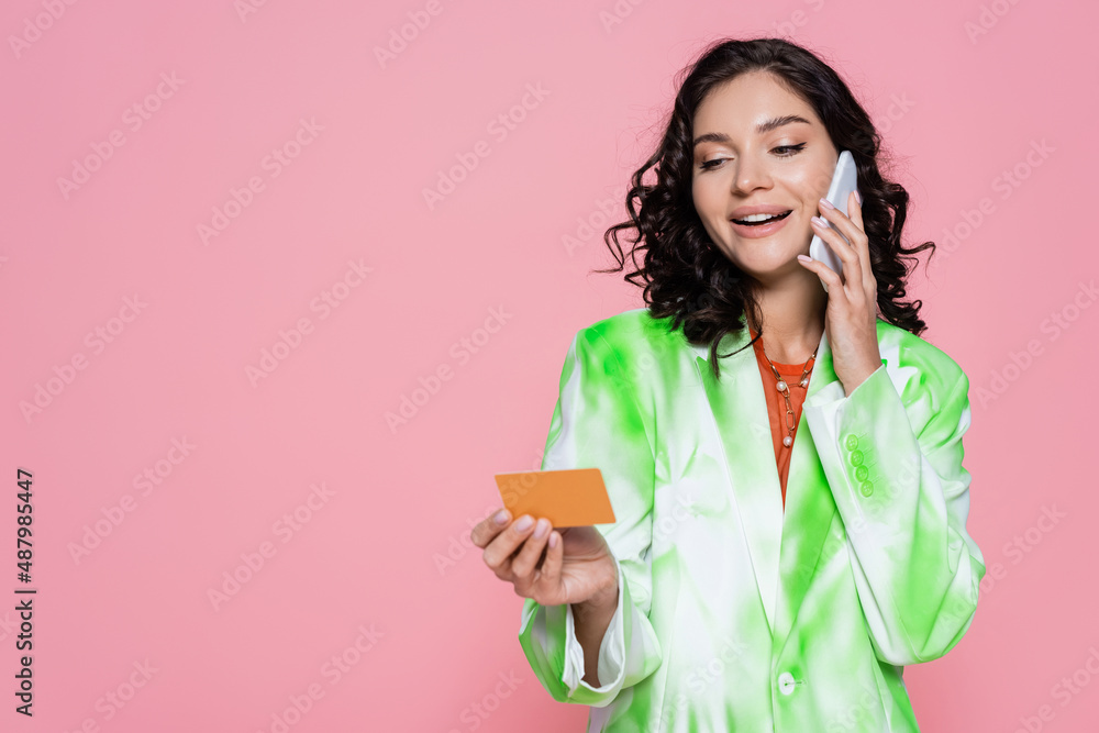 happy young woman in tie dye blazer holding credit card and talking on smartphone isolated on pink. happy young woman in tie dye blazer holding credit card and talking on smartphone isolated on pink.