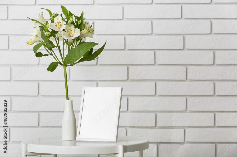 Vase with beautiful flowers and photo frame near white brick wall Vase with beautiful flowers and photo frame near white brick wall