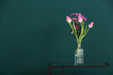 Vase with beautiful flowers on table near green wall