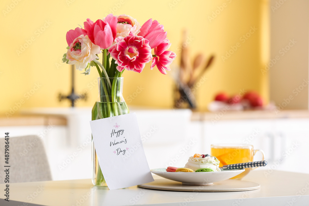 Vase with flowers, breakfast and greeting card with text HAPPY WOMEN'S DAY on dining table in kitchen