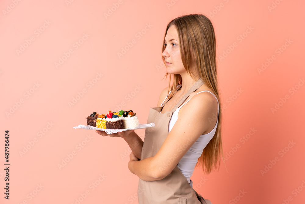 Pastry Ukrainian chef holding a muffins isolated on pink background looking side Pastry Ukrainian chef holding a muffins isolated on pink background looking side