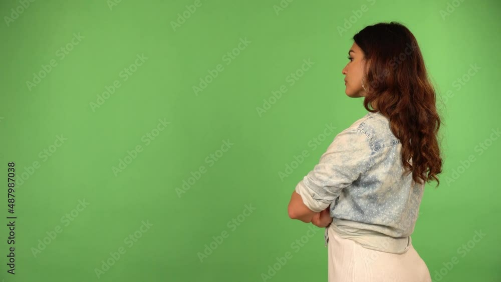 A young beautiful Caucasian woman looks around as she faces the green screen background A young beautiful Caucasian woman looks around as she faces the green screen background