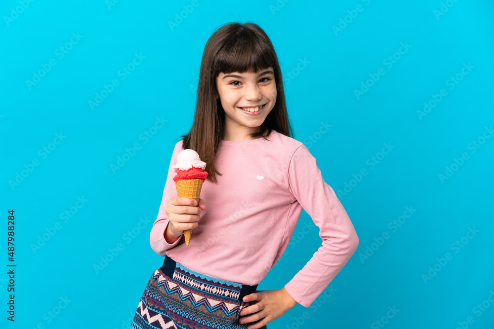 Little girl with a cornet ice cream isolated on blue background posing with arms at hip and smiling Little girl with a cornet ice cream isolated on blue background posing with arms at hip and smiling