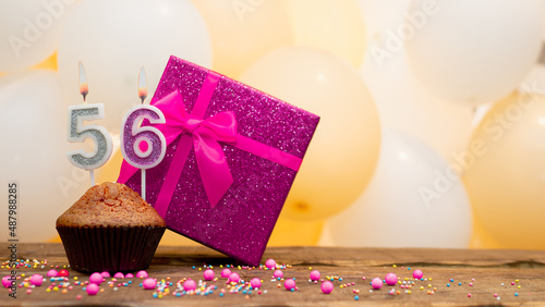 Happy birthday with a pink gift box for a 56 year old woman. Beautiful birthday card with cupcake and burning candle number fifty six.