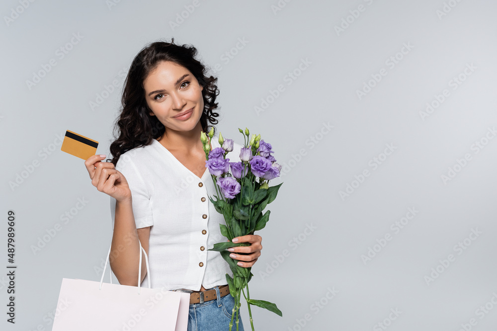 pleased woman holding bouquet of flowers, shopping bag and credit card isolated on grey. pleased woman holding bouquet of flowers, shopping bag and credit card isolated on grey.