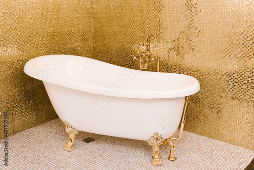 Beautiful white freestanding bathtub next to the golden tile on the wall