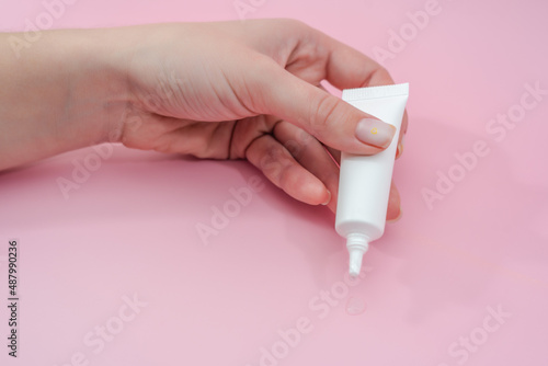 Female hand squeezes cream or gel from tube on pink background. Сosmetic bottles for beauty or medicine products