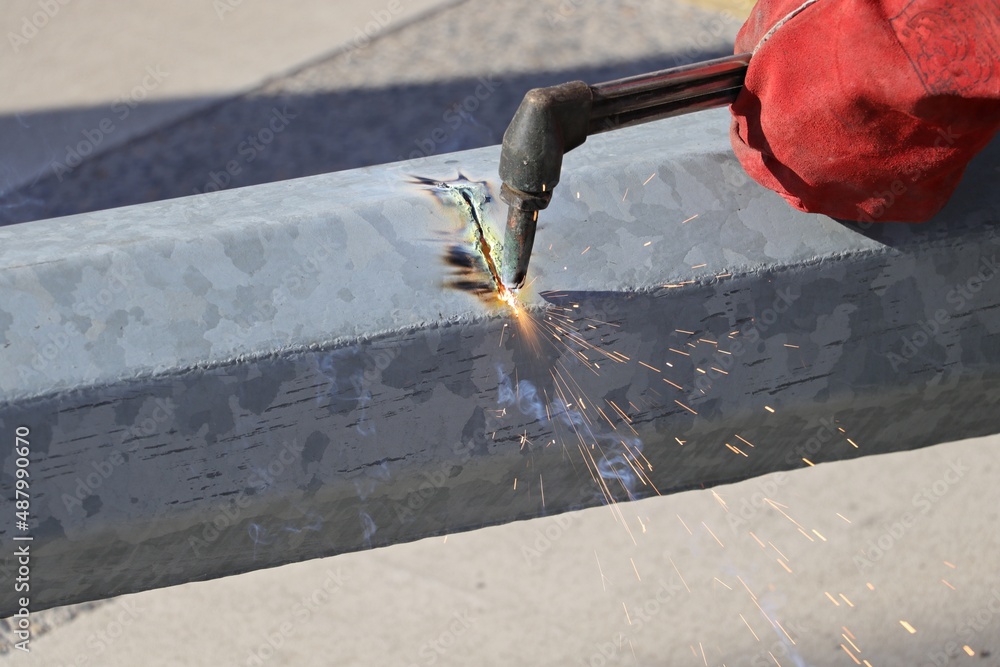 Male hand in red glove cutting the overturned lamppost with a blowtorch
