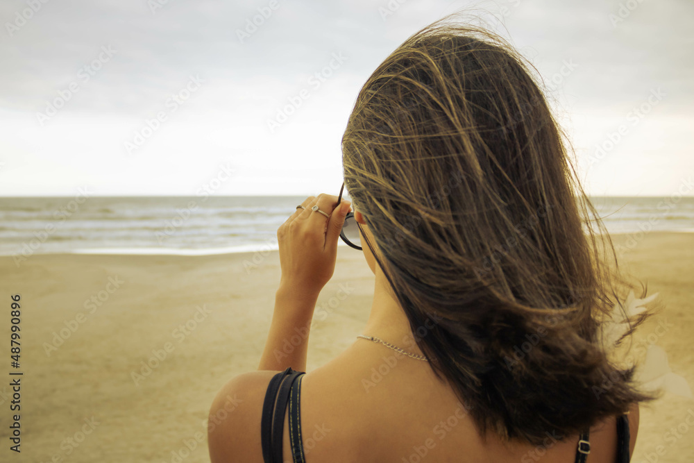 Girl looking towards the sea on an access walkway amidst the dunes. Putting on sunglasses. Mention the beach, vacations and rest. Beautiful women in the late afternoon sun. Girl looking towards the sea on an access walkway amidst the dunes. Putting on sunglasses. Mention the beach, vacations and rest. Beautiful women in the late afternoon sun.