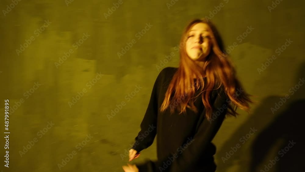 Choreography of modern dance. Funny young woman with long hair dances hip hop, freestyle in the dance hall under a flashing bright studio light. Shot from the point of view.