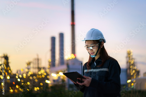 Photography Asian woman petrochemical engineer working at night with digital tablet Inside oil and gas refinery plant industry factory at night for inspector safety quality control