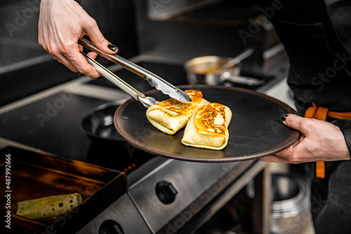 chef hand cooking Thin pancakes crepe rolls with ground meat in pan at a restaurant kitchen