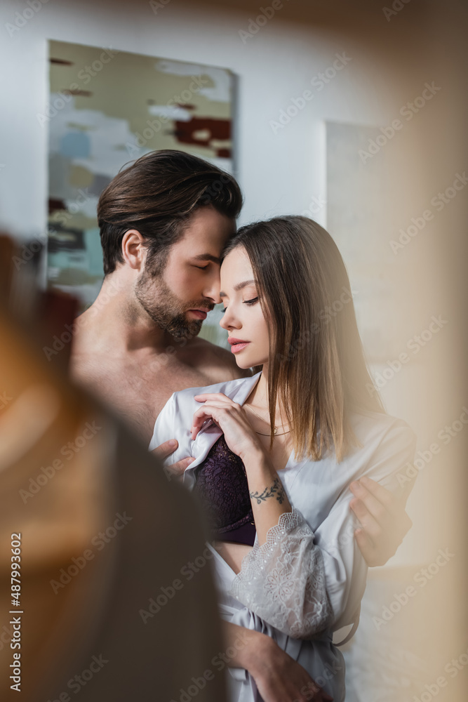 shirtless man undressing tattooed woman in silk robe. shirtless man undressing tattooed woman in silk robe.
