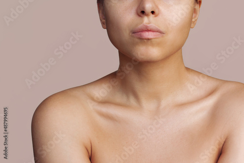 Photos Cropped shot of a young caucasian tanned woman with a protruding collarbone isolated on a beige background