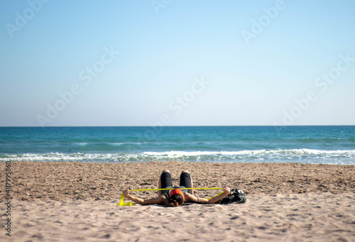 Fototapeta Naklejka Na Ścianę i Meble -  Adult woman exercising with rubber bands on the beach lying down on the beach