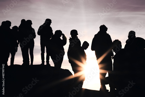 Low angle silhouette shot of a group of people watching the sunset on a hill against the sun