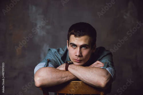 Portrait. Young man with a short hair in a turquoise shirt sit on a chair and looking away the camera. High quality photo © Людмила Гилева