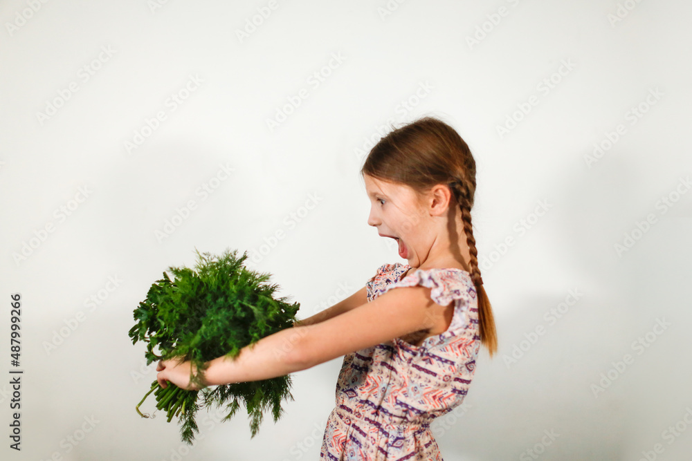 Funny caucasian girl child with bouquets of greenery on a light background, vegetables and vitamins for children. Strong child healthy food, bunches of parsley and dill Funny caucasian girl child with bouquets of greenery on a light background, vegetables and vitamins for children. Strong child healthy food, bunches of parsley and dill