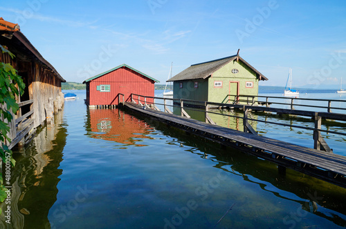 a long wooden pier leading to the colorful boat houses on lake Ammersee in the German fishing village Schondorf (Ammersee, Germany) 