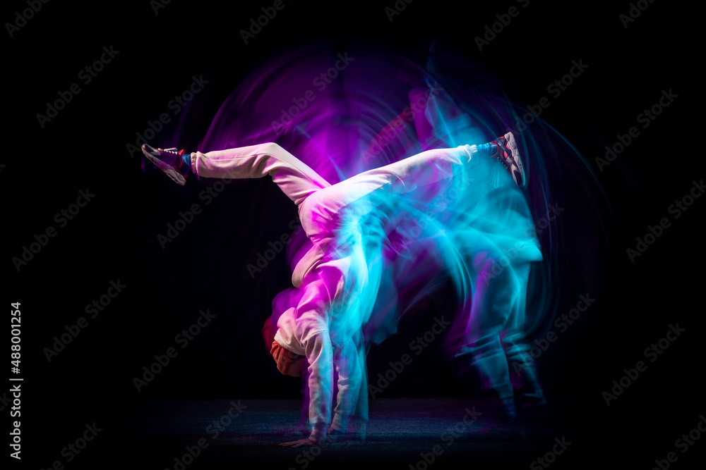 Hand stand. One energy young flexible sportive man dancing hip-hop or breakdance in white outfit on dark background in mixed blue neon light. Sport, art, action, moves Hand stand. One energy young flexible sportive man dancing hip-hop or breakdance in white outfit on dark background in mixed blue neon light. Sport, art, action, moves