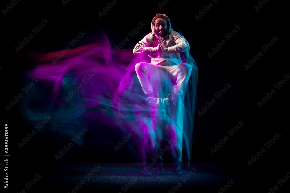 One energy young flexible sportive man dancing hip-hop or breakdance in white outfit on dark background in mixed blue neon light. Sport, art, action, moves