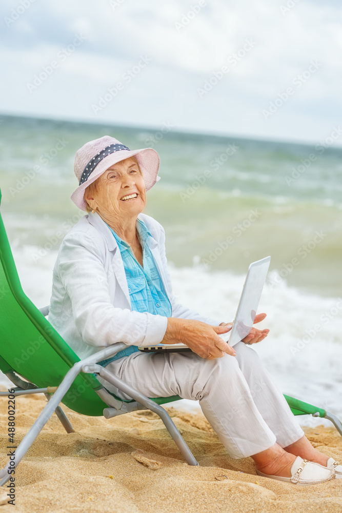 Very old wrinkled woman with a laptop on the seashore.
