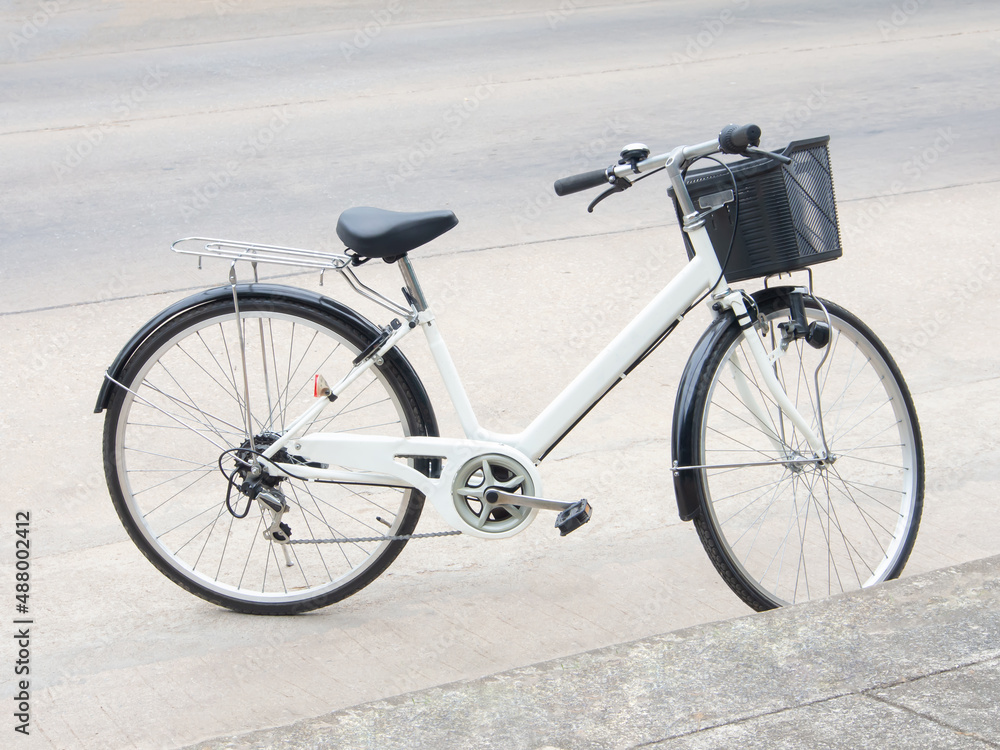 white vintage style bicycle with thin tire and black basket park on cement road floor