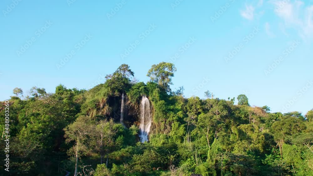 A wide view of the natural waterfall that flows down the mountain is lit by the evening sun in Thailand. Slow motion. A wide view of the natural waterfall that flows down the mountain is lit by the evening sun in Thailand. Slow motion.