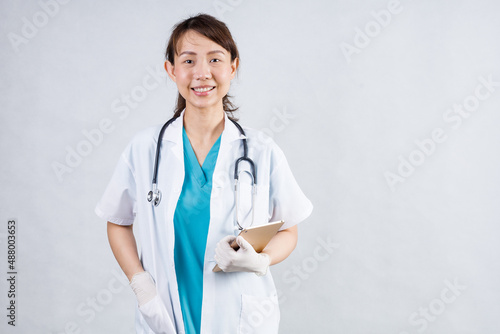 Smiling asian woman physician in a white coat over gray background