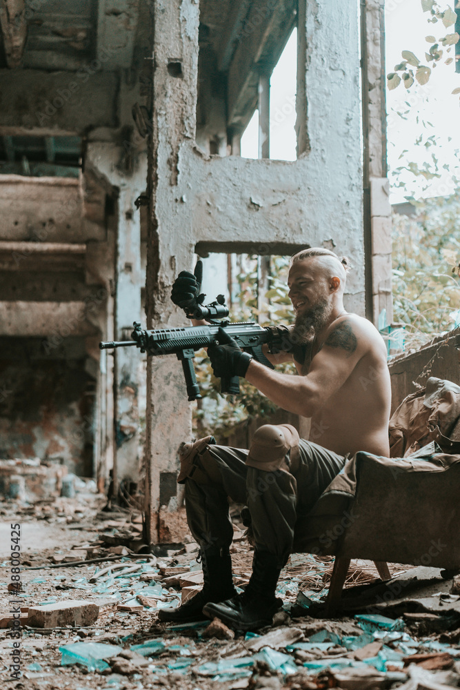 Fototapeta premium a male military soldier in an abandoned building with a gun poses, shoots and takes aim