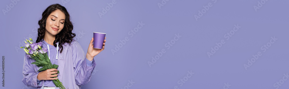 happy young woman in raincoat holding bouquet of flowers and paper cup isolated on purple, banner. happy young woman in raincoat holding bouquet of flowers and paper cup isolated on purple, banner.