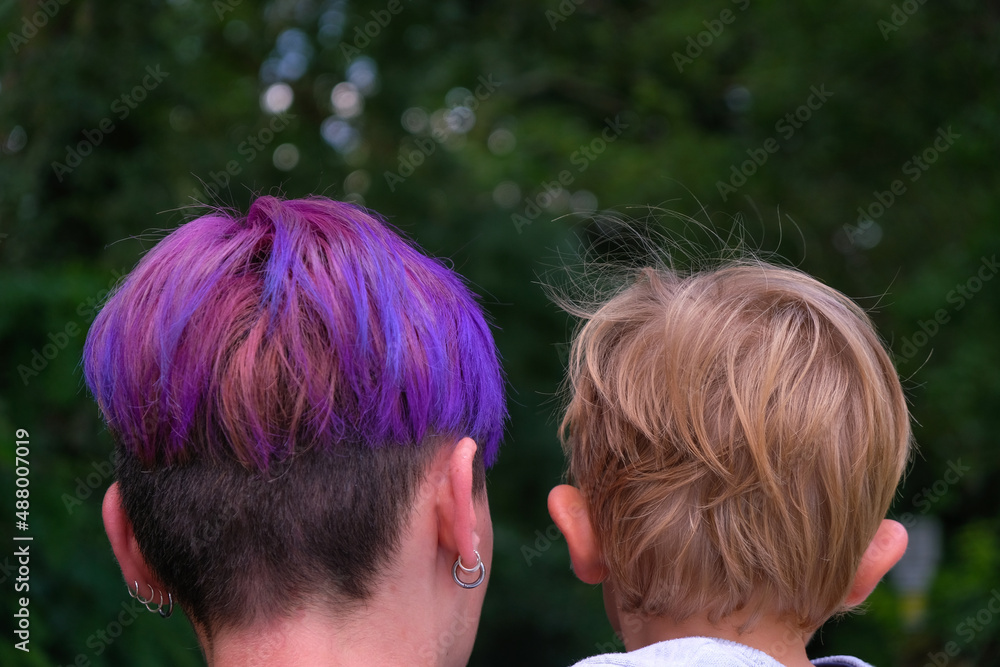 The head of a young woman with purple hair and the blond head of a baby. Family walk in the park. Happy childhood concept. Rear view. The head of a young woman with purple hair and the blond head of a baby. Family walk in the park. Happy childhood concept. Rear view.