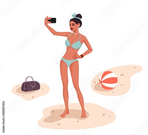 Woman taking a selfie on the beach. Pretty young woman in bikini, standing on seacoast sand and shooting smartphone self portrait on beach, posting vacation travel selfie photos to social media, blog