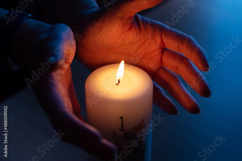 Burning candle with number 1 and hands warming near flame