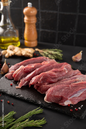 Pieces of fresh pork meat on a black table close up, raw meat with seasoning for cooking on a black board vertical photo