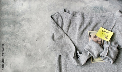 SPEND LESS. gray cotton T-shirt on a gray background with dollars and a sticker with the inscription 