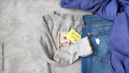 SPEND LESS. Casual comfortable clothes: blue jeans, gray cotton T-shirt, blue scarf on a gray background with a place for text. The concept of a second-hand wardrobe, thrifty shopping, be economical.