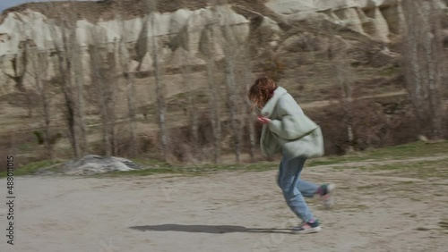 Happy girl running to mother in sandy valley in Cappadocia. Woman with smartphone taking pictures of cheerful teenage daughter running in valley in Cappadocia, Turkey photo