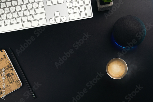 Home office. Modern black table with white keyboard, hot coffee, notepad, virtual assistant on the side. Space for text. Top view