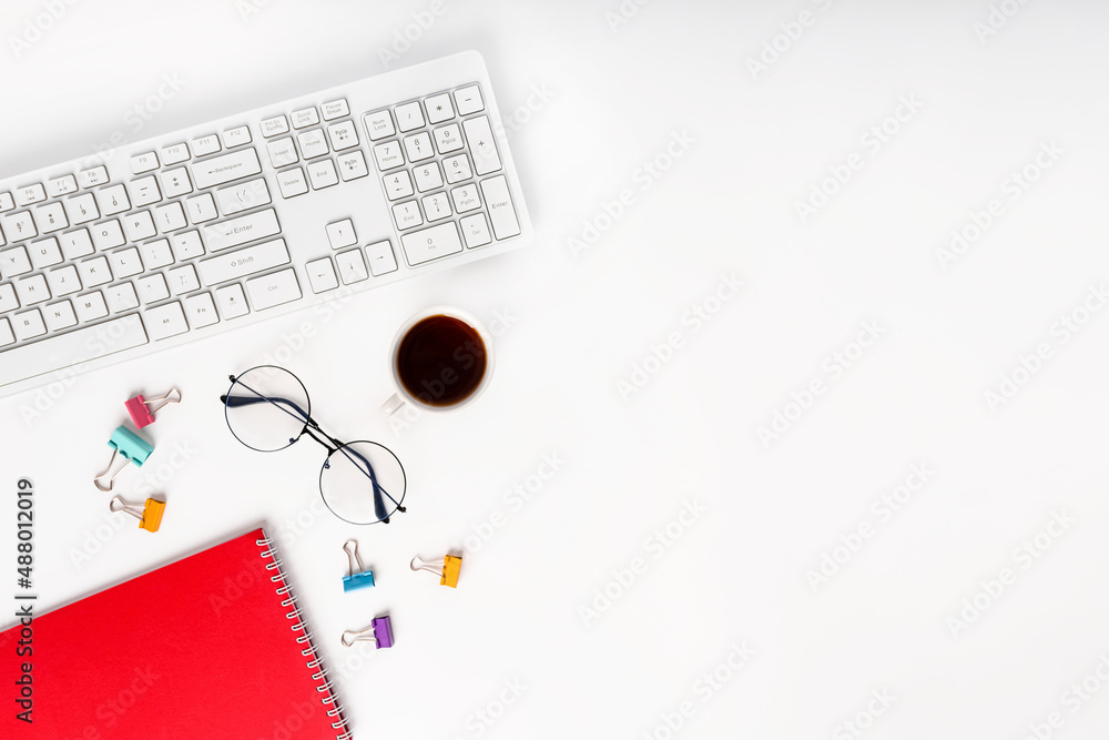Fototapeta premium Top view of a modern office desk with a notepad, glasses, keyboard and a coffee or tea cup on a white background with a place for text