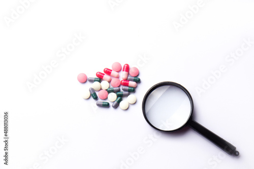 Vitamin tablets and a magnifying glass on a white background. Dietary supplements and pills for dieting. Medical concept. Complementary and medical products