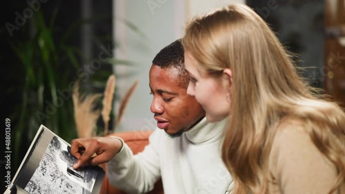 African-American man shows faded photo and tells about grandfather to white lady coworker in living room during visit closeup slow motion photo