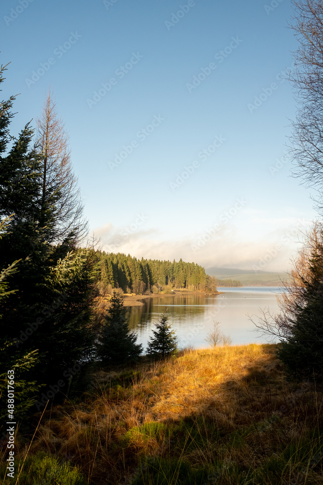 Kielder England: 11th January 2022: Warm sun shining on a view of lake (Kielder reservoir) with trees in silhouette. Kielder England: 11th January 2022: Warm sun shining on a view of lake (Kielder reservoir) with trees in silhouette.